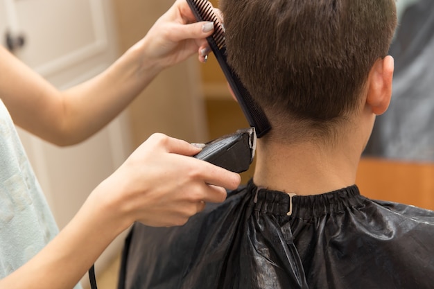 Master cuts hair of men in the barbershop, hairdresser makes hairstyle for a young man.