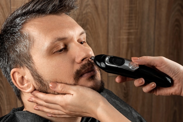 Master cuts nose hair to client with trimmer, close-up. The process at the hairdresser, barbershop. Body care, lifestyle, metrosexual.