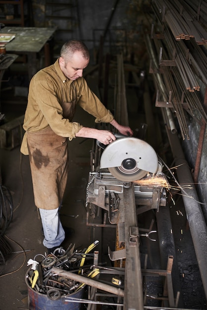 The master cuts a piece of metal on a circular saw in the workshop