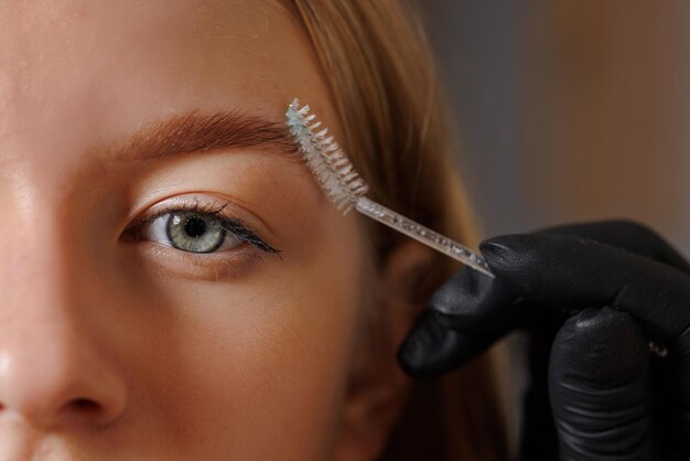 Foto master eyebrowist maakt wenkbrauwcorrectie aan een meisje in een schoonheidssalon closeup