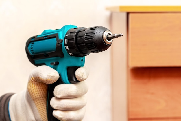 The master holds in his hand cordless screwdriver near the cabinet