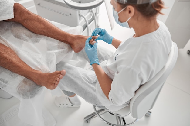 Фото Мастер в синих перчатках проверяет ногти мужчины перед процедурой в салоне красоты