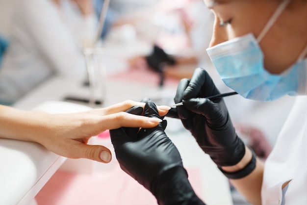 Master in handschoenen werkt met nagels, manicure procedure in de schoonheidssalon.