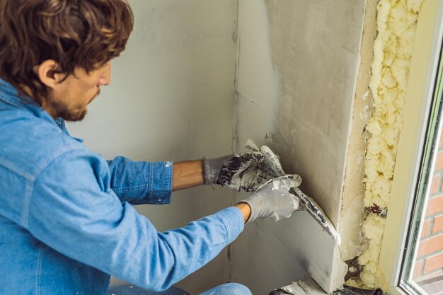 Master is applying white putty on a wall and smearing by putty knife in a room of renovating house in daytime