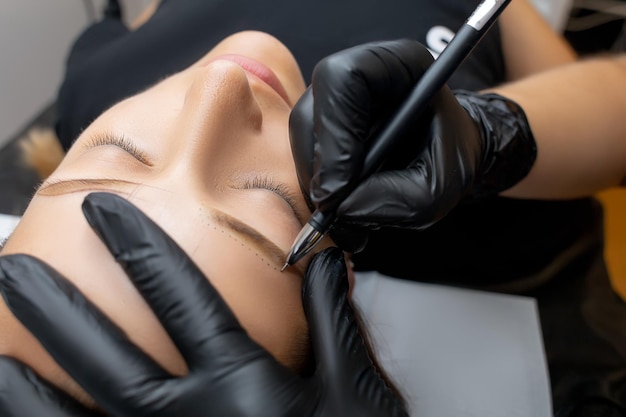 The master makes a contour with a pencil before the eyebrow tattoo procedure permanent makeup