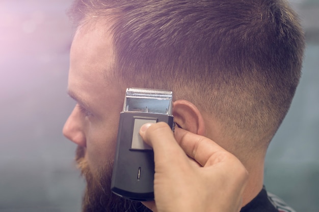 Master makes a stylish haircut to a young guy in a barbershop