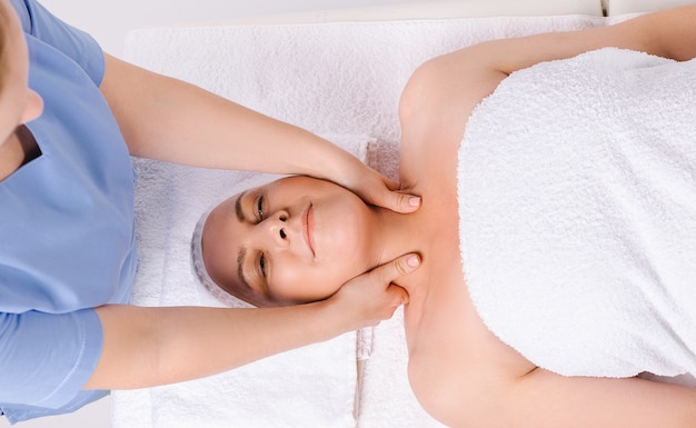 The master masseur is giving a relaxing head and neck massage to an older woman wrapped in a white