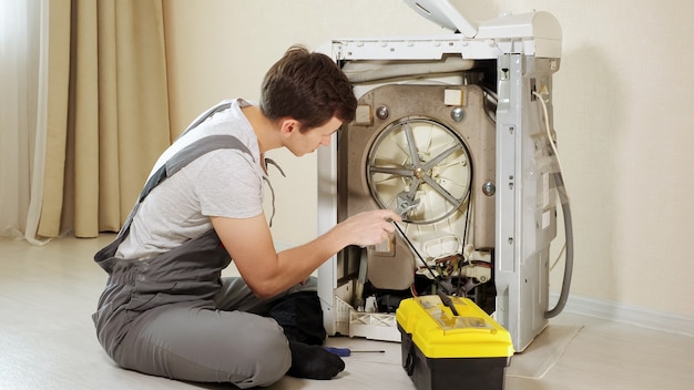 Master opens back panel of broken washing machine near wall