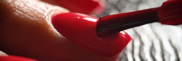 Master painting nails with bright red varnish to client closeup