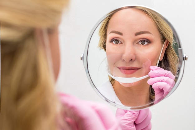 Photo master of permanent make-up in a mask on his face looks in the mirror