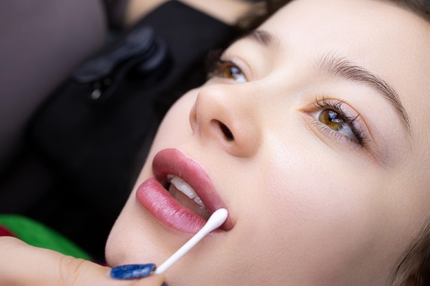 The master of permanent makeup evenly distributes oil on the lips of the model with a cotton swab after the tattoo procedure
