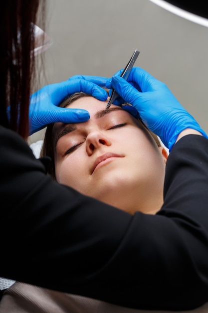 Photo the master plucks out the excess hairs on the eyebrows with tweezers, giving them a shape.