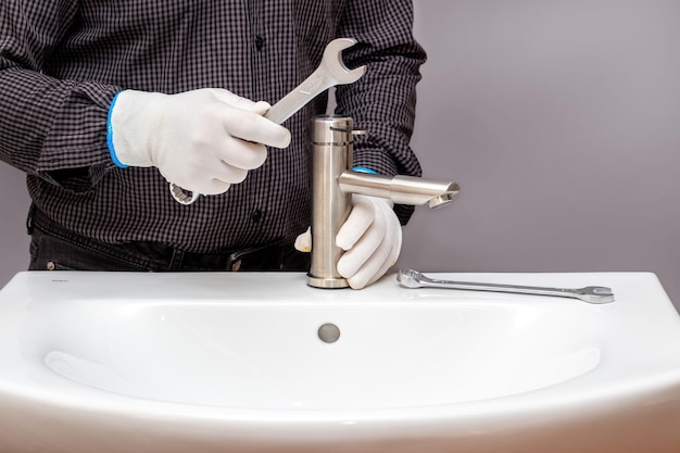 A master plumber with a wrench in his hand screws the faucet to\
the sink in the bathroom