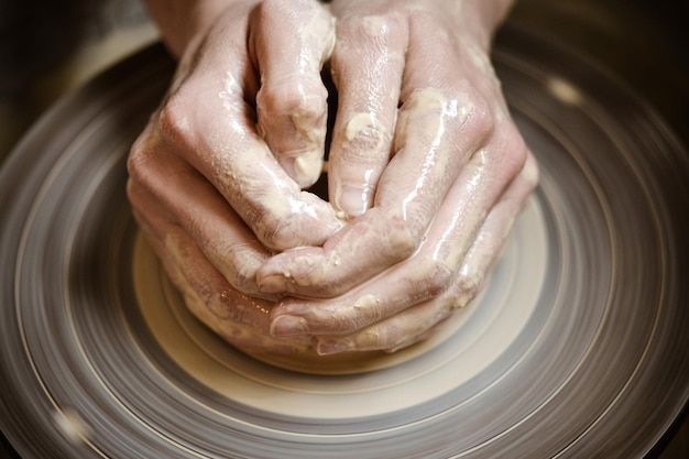 Foto il maestro ceramista, con le mani piegate, scolpisce un prodotto in argilla su una ruota di ceramica in primo piano