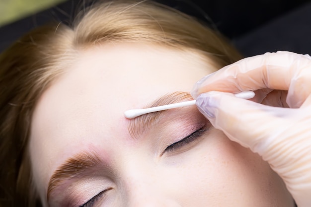Photo the master removes excess laminating composition from the contour of the eyebrows with a cotton swab