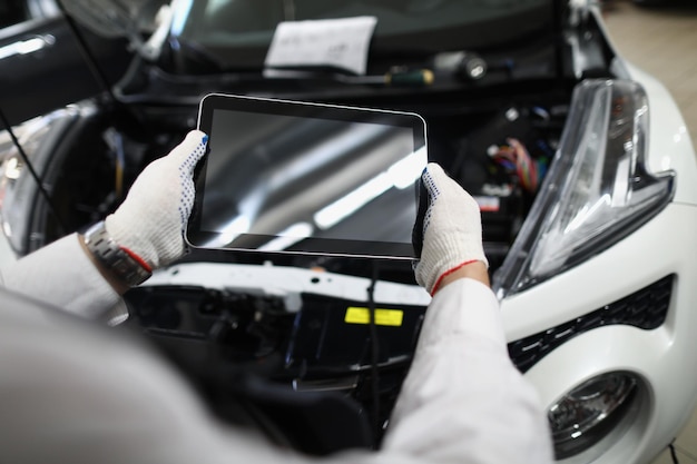 Master repairman holding digital tablet near open hood of car closeup