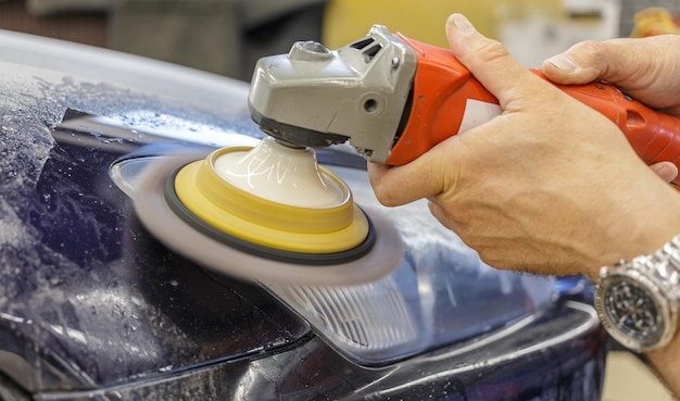 Master repairman polishing headlights of car in workshop using machine closeup