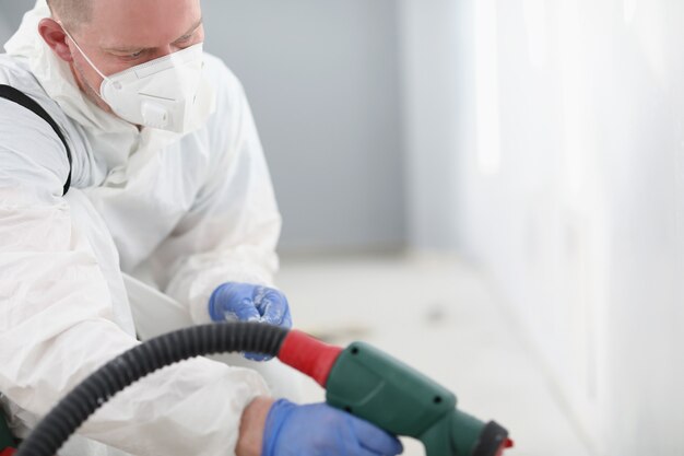 Master repairman in protective respirator and uniform painting wall with spray gun