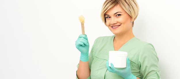 The master of sugar hair removal holds liquid yellow sugar paste wax for depilation with the jar on a wooden stick on a white background