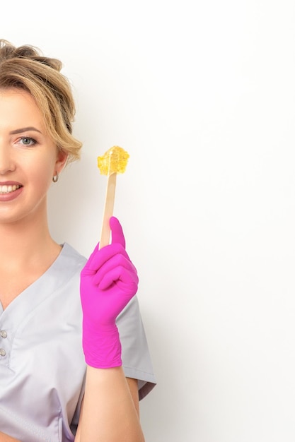 The master of sugar hair removal holds liquid yellow sugar paste wax for depilation on a wooden stick on a white background
