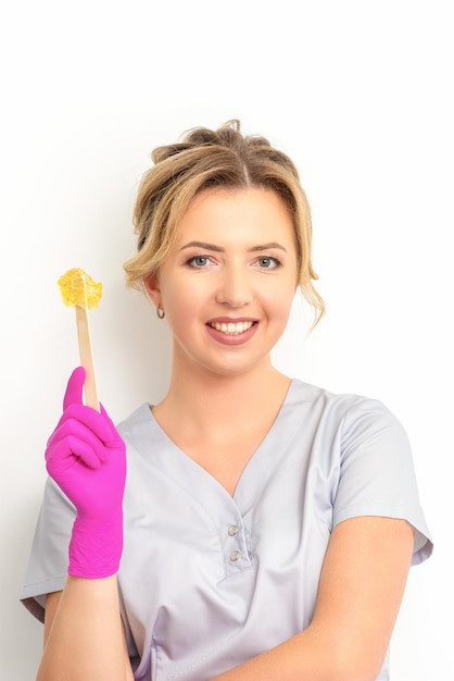 The master of sugar hair removal holds liquid yellow sugar paste wax for depilation on a wooden stick on a white background