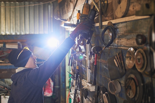 Master takes the electric saw with wooden wall with tools