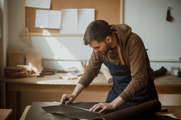 Master tanner cuts piece of leather in workshop