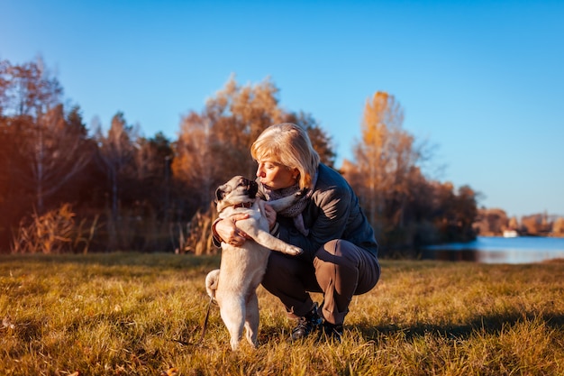 Master walking pug dog in autumn park by river Happy woman kissing pet