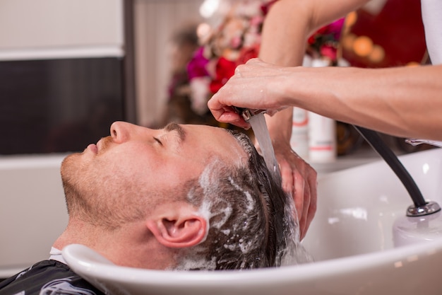 Master washes the head of the client in the Barber shop, hairdresser makes hairstyle for a young man.