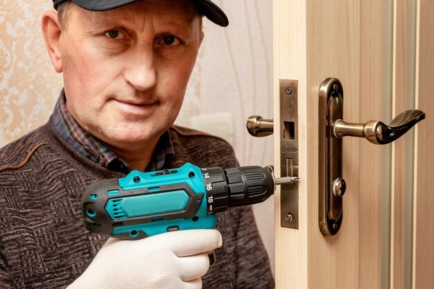 A master with an electric screwdriver repairs the door lockxA