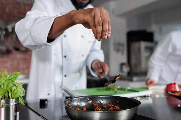 Masterchef-kruidenschotel bereid voor voedselwedstrijd gehouden in fine dining restaurant. Hoofdkok die verse gehakte kruiden in de pan gooit om de smaak van de maaltijd te verbeteren in de professionele keuken.