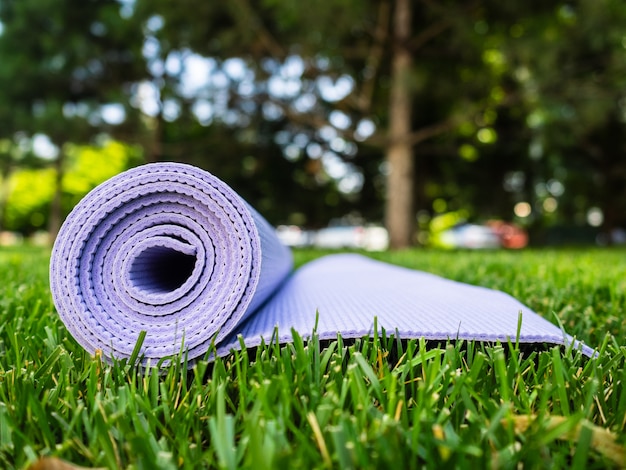 Mat voor yoga of fitness. Purper tapijt op groen gras in de schaduw van een boom