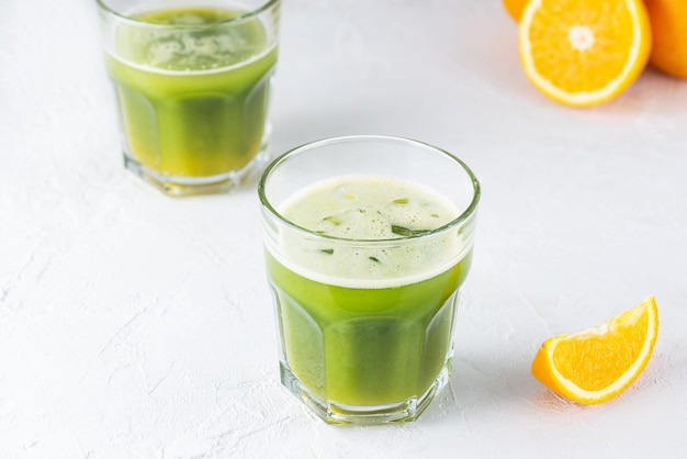 Matcha drink and orange juice with ice in glasses on a light background.