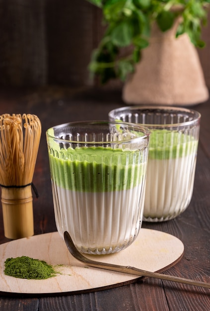 Matcha green latte tea, matcha powder and bamboo whisk on wood