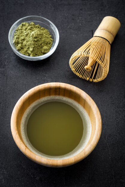 Matcha green tea in a bowl and bamboo whisk on black slate