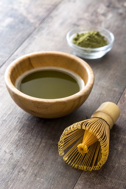 Matcha green tea in a bowl and bamboo whisk on wood