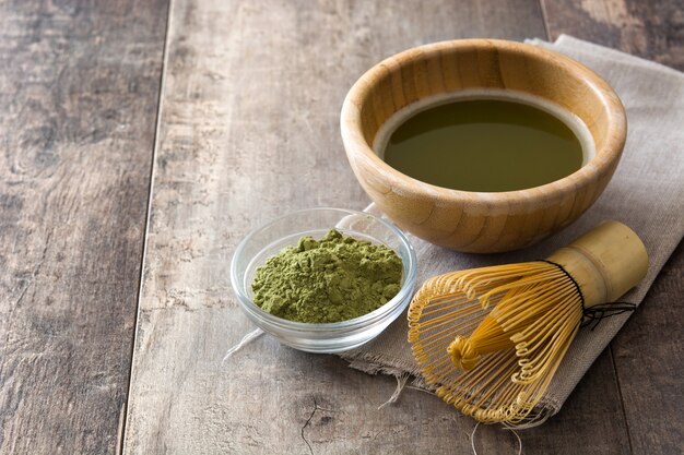 Matcha green tea in a bowl and bamboo whisk on wood