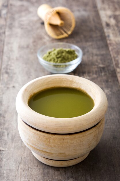 Matcha green tea in a bowl and bamboo whisk, on wooden table