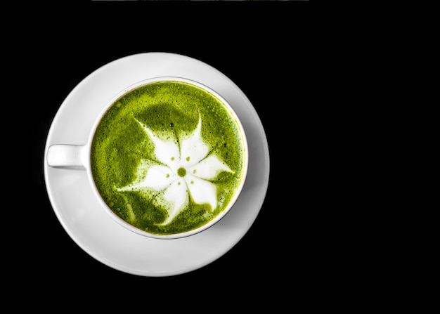 Matcha green tea latte art in cup on white saucer against black background