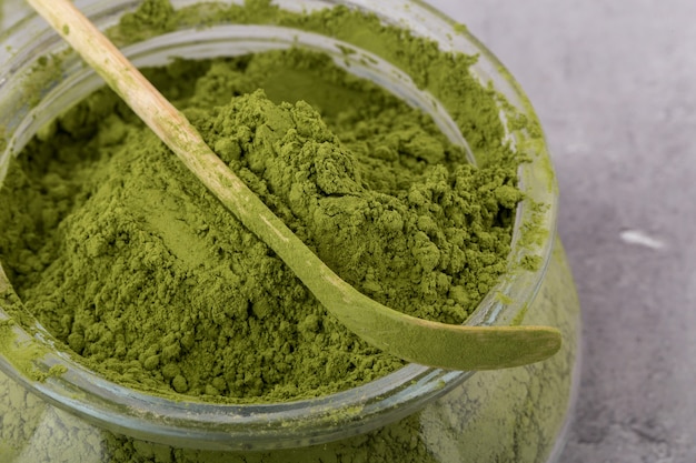 Matcha green tea powder, in a glass container, with a special wooden spatula, gray background, close up