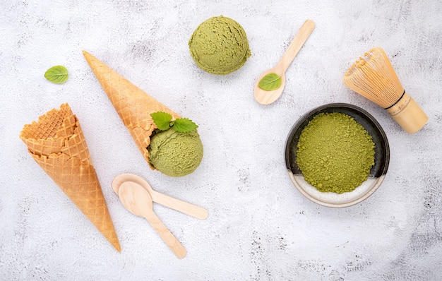 Matcha groene thee-ijs met wafelkegel en muntblaadjes setup op witte stenen achtergrond.