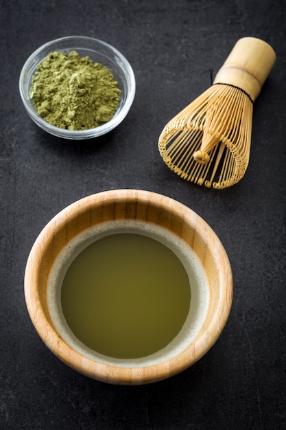 Matcha groene thee in een kom en bamboe zwaaien op zwarte leisteen