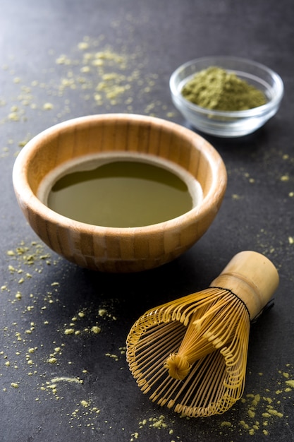 Matcha groene thee in een kom en bamboe zwaaien op zwarte leisteen
