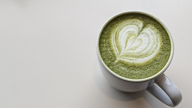 Matcha latte in een keramische beker met hartschuim de foto benadrukt een bekertafel en een hartpatroon