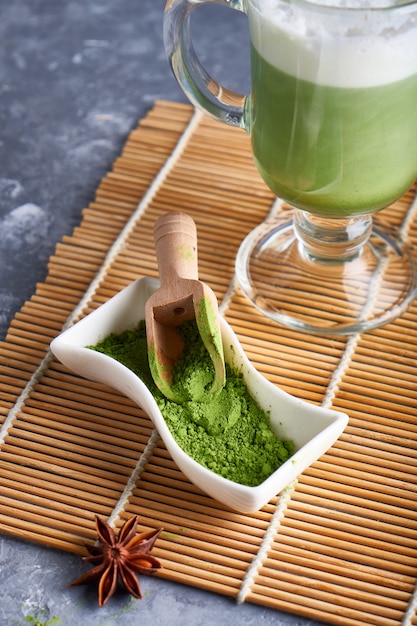 Matcha-poeder in groene thee in kom en Matcha Latte op grijze tafel