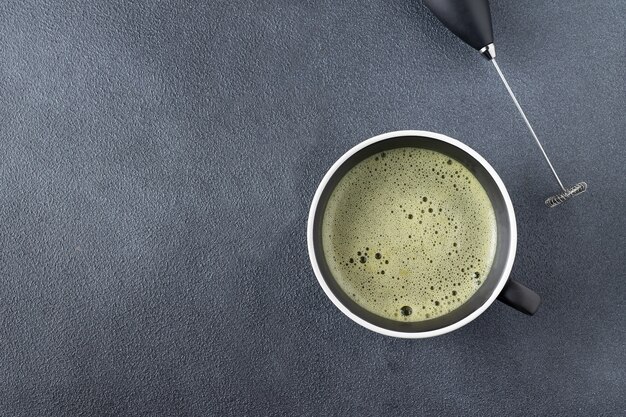 Matcha-thee en cappuccinator in een mok op een zwarte achtergrond