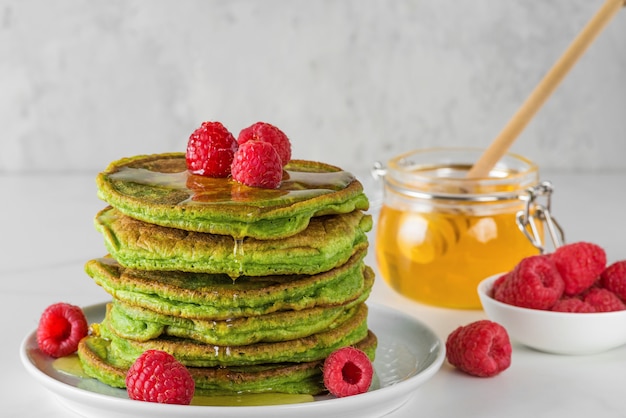 Matcha thee groene pannenkoeken. Stapel zelfgemaakte pannenkoeken met verse frambozen en honing. gezond ontbijtdessert