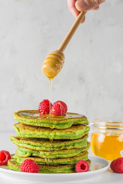 Matcha thee groene pannenkoeken. Stapel zelfgemaakte pannenkoeken met verse frambozen en vloeiende honing. verticale oriëntatie