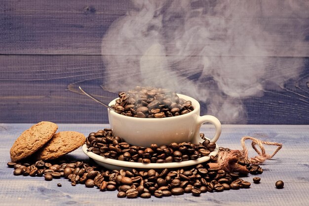 Mate van gebrande granen Kop vol koffie bruin gebrande bonen witte rookwolken blauwe houten ondergrond Cafe drankenkaart Vers gebrande koffiebonen Koffie voor inspiratie en energie lading