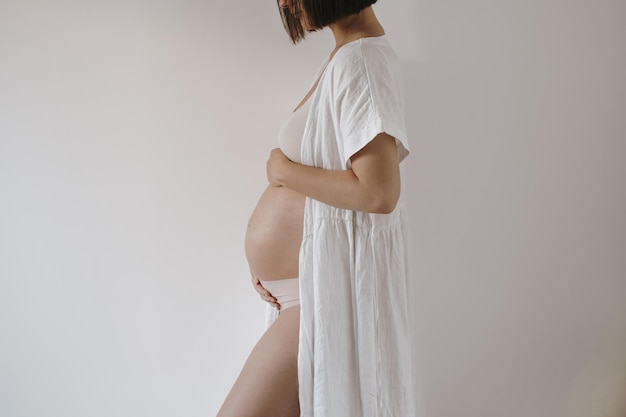 Maternity happiness concept Young pretty happy pregnant woman in elegant white dress touch tummy Minimalist aesthetic pregnancy